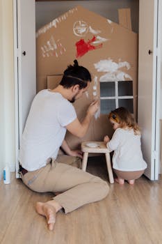 Father and daughter painting a cardboard house indoors, enjoying quality time together. Canada Wide Rent Buy Homeownership Strategy