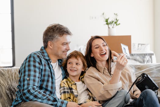 A cheerful family enjoys time together on a couch surrounded by moving boxes in their new home. Own Your Home Through Monthly Rent Payments Canada