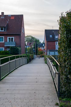 A serene suburban pathway lined with bushes and modern homes, captured at dusk