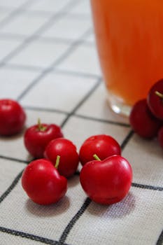 Fresh acerola cherries and a glass of juice on a patterned tablecloth. Perfect for healthy lifestyle concepts.