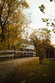 Picturesque autumn view of a rustic bridge and cottage surrounded by vibrant fall foliage.