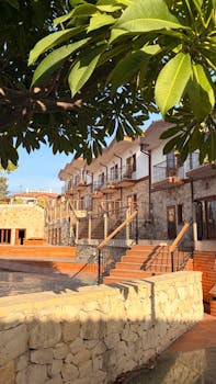 Rustic stone villas beneath lush trees under a sunny sky, showcasing architectural charm.